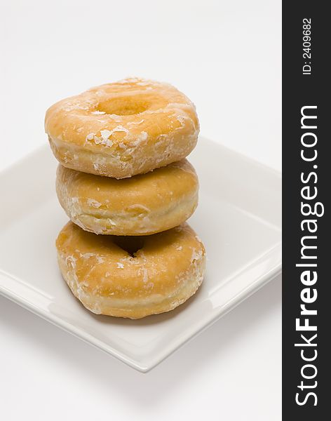 Three glazed donuts stacked on white plate