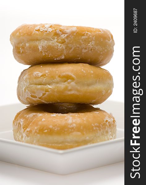 Three glazed donuts stacked on white plate side view