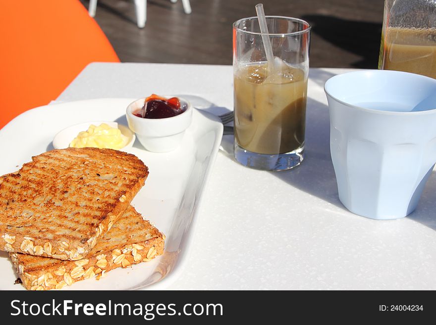 A simple breakfast served at a cafe: two wholemeal toasts with butter and raspberry jam, a cup of tap water and a healthy green juice. A simple breakfast served at a cafe: two wholemeal toasts with butter and raspberry jam, a cup of tap water and a healthy green juice