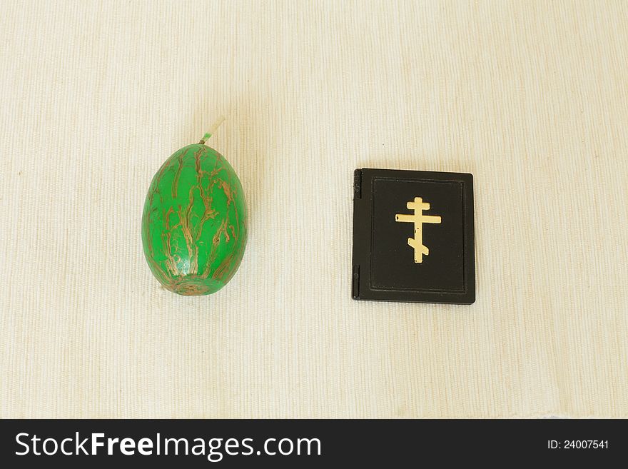 Candle in the form of Easter egg green close-up on the table next to the image of an Orthodox cross. Candle in the form of Easter egg green close-up on the table next to the image of an Orthodox cross.