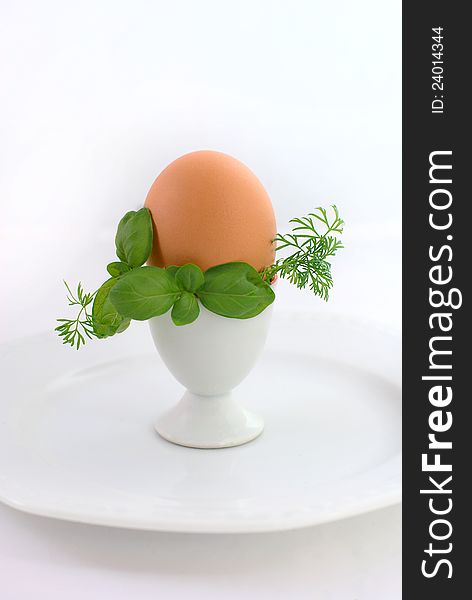 Egg in eggcup on the white plate, decorated with greenery