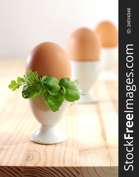 Egg in eggcup on the wooden desk, decorated with greenery. Egg in eggcup on the wooden desk, decorated with greenery