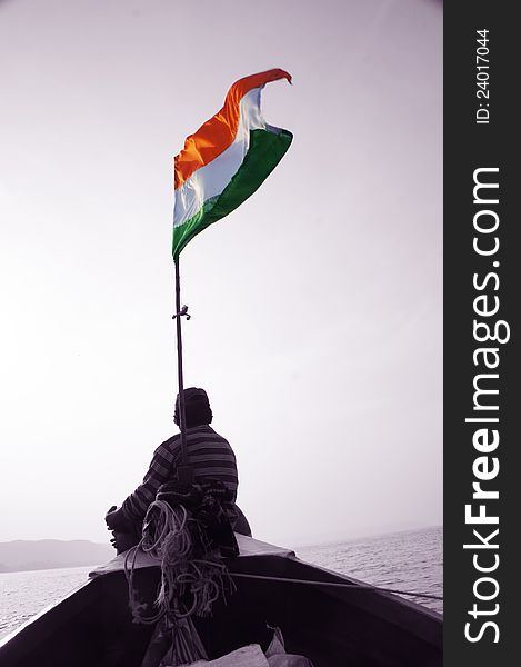 A young man facing the sea, sitting on a boat, which has an Indian Tri-color flag. A young man facing the sea, sitting on a boat, which has an Indian Tri-color flag.