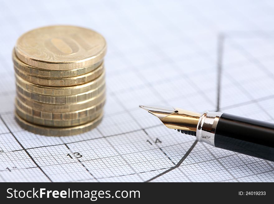 Business concept. Closeup of fountain pen near stack of coins on graph paper with diagram. Business concept. Closeup of fountain pen near stack of coins on graph paper with diagram