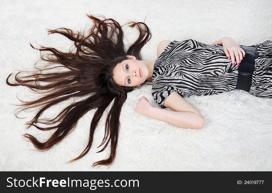 Beautiful girl with long hair wearing striped dress lies on white fur in studio. Beautiful girl with long hair wearing striped dress lies on white fur in studio