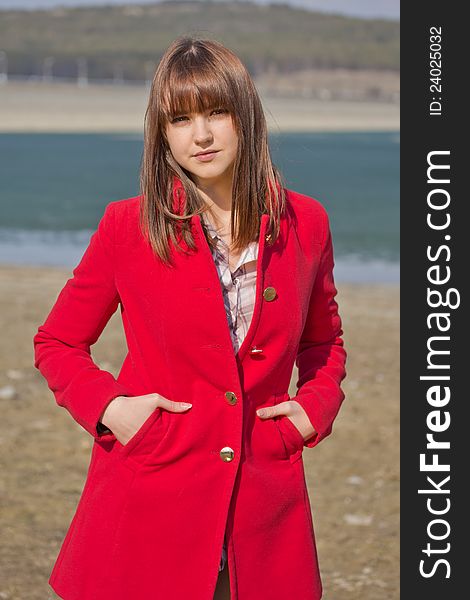 Young girl in red coat stands on the beach