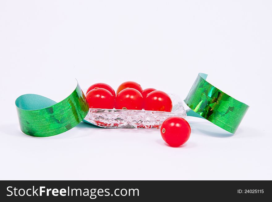 Little red tomatoes, green ribbon, in a small crystal vase on white. Little red tomatoes, green ribbon, in a small crystal vase on white.