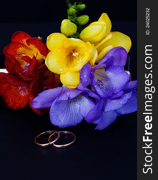 Wedding rings and a bouquet of freesias on a black background