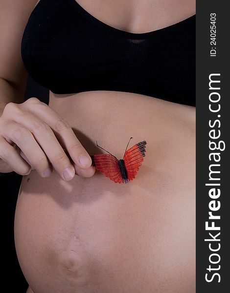 Hand of a pregnant woman holding a red butterfly on her tummy. Hand of a pregnant woman holding a red butterfly on her tummy