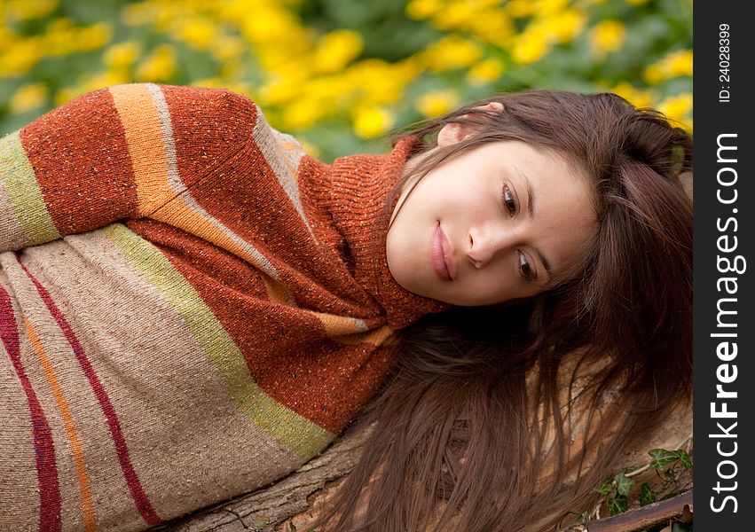 A portrait of a pretty young woman, looking thoughtful as she lies on a log with flowers in the background. A portrait of a pretty young woman, looking thoughtful as she lies on a log with flowers in the background