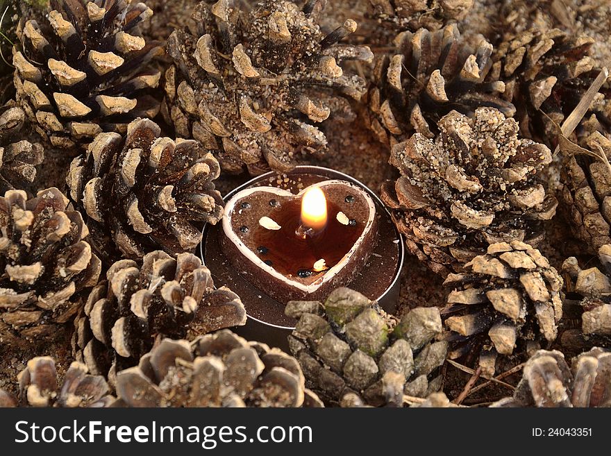 A heart shaped candle surronding by pine cones. A heart shaped candle surronding by pine cones