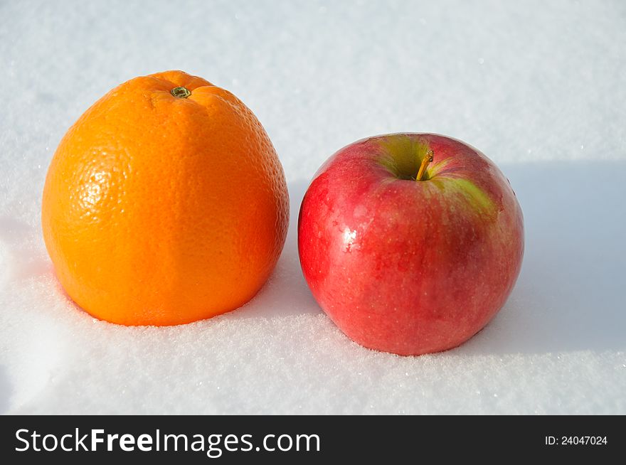 The image of apple and orange on clean snow