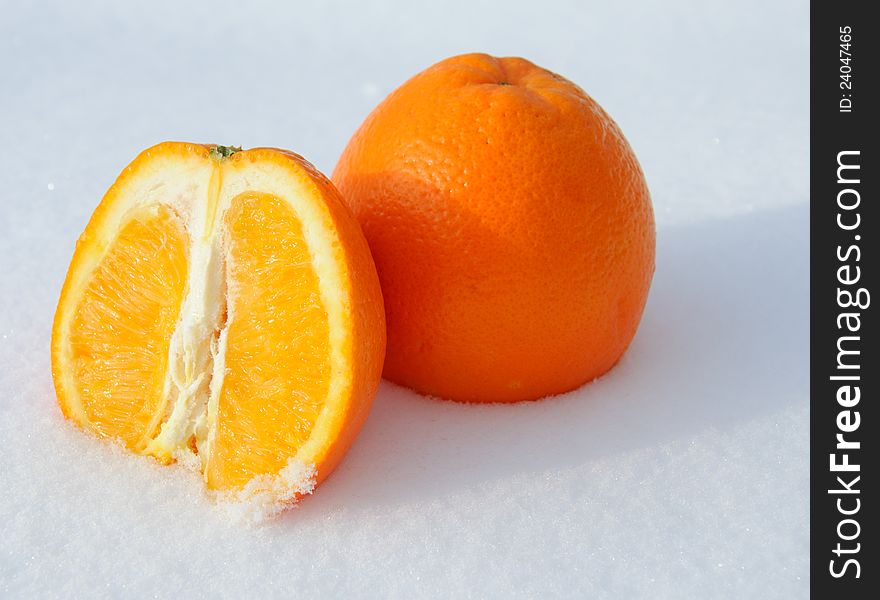 Close-up of pieces of cut orange in white snow and with sun light