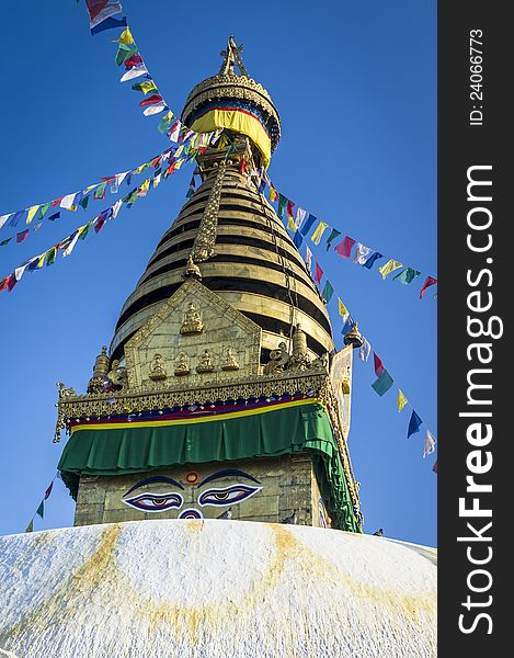 Buddha stupa in Kathmandu with buddha eyes and prayer flags on clear blue sky.