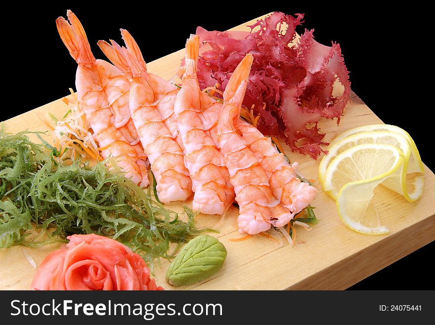 Sashimi eb with shrimps, lemon lobules, ginger, wasabi, red and green algae on rectangular board isolated on a black background. Sashimi eb with shrimps, lemon lobules, ginger, wasabi, red and green algae on rectangular board isolated on a black background