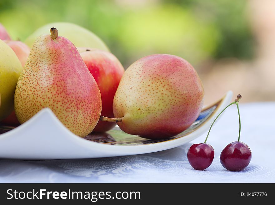 Still life with a plate of pears and a pair of cherries on a white tablecloth. Still life with a plate of pears and a pair of cherries on a white tablecloth