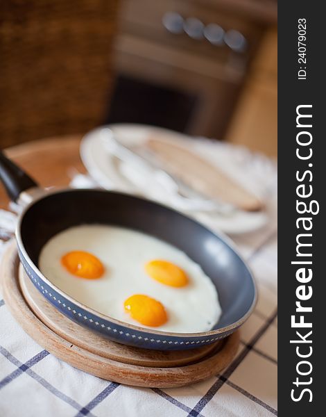 Picture of three fried eggs in a pan, standing on a kitchen table