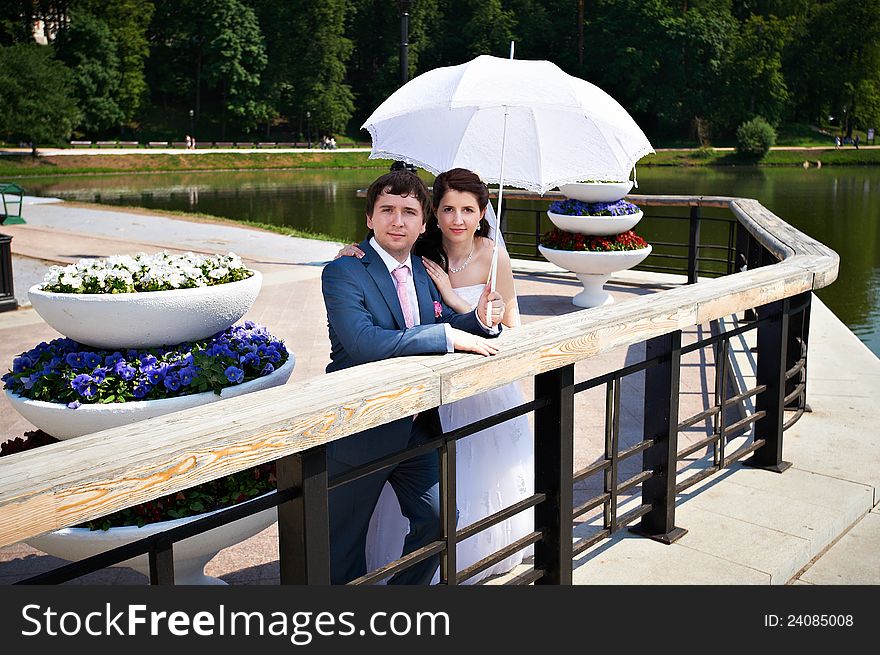 Happy bride and groom with umbrella on park