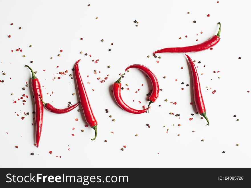 Red chili peppers shaping the word hot, surrounded with peppercorns, isolated on white background. Red chili peppers shaping the word hot, surrounded with peppercorns, isolated on white background