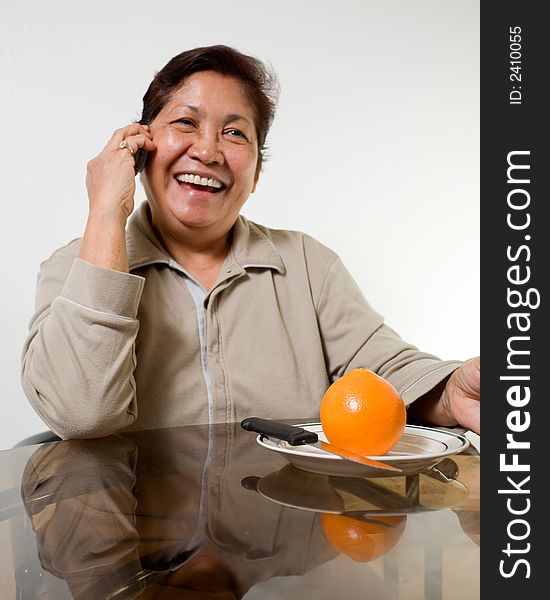 Portrait of a senior asian woman smiling sitting at the kitchen table about to peel and orange. Portrait of a senior asian woman smiling sitting at the kitchen table about to peel and orange