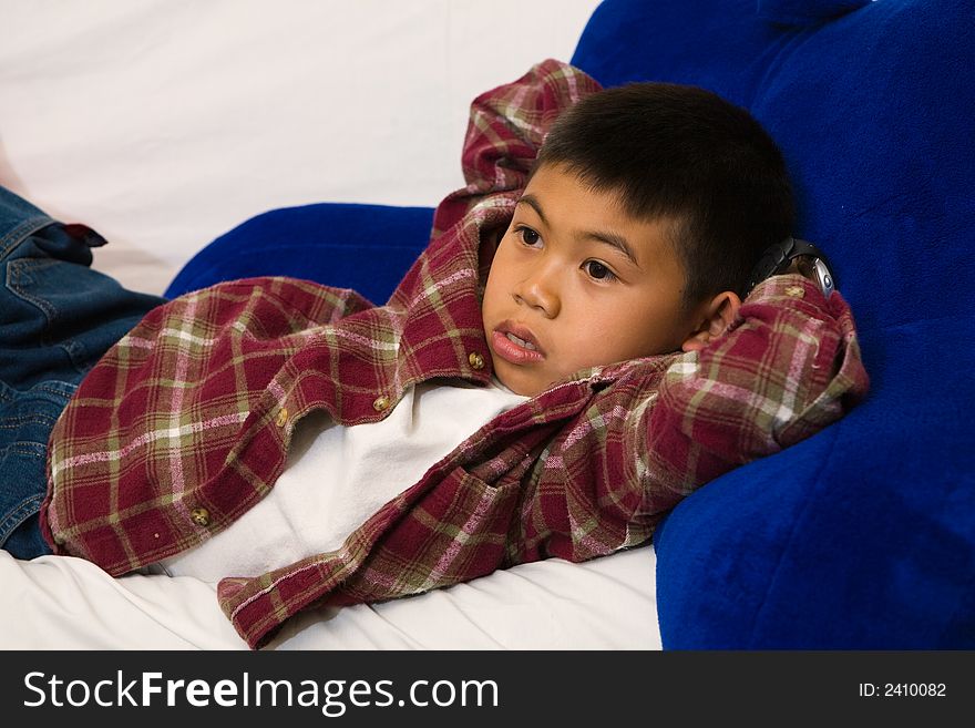 Young asian boy laying down on a sofa while looking engrossed in the television. Young asian boy laying down on a sofa while looking engrossed in the television