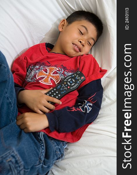 Young asian boy comfortably laying down on the sofa holding the television remote control. Young asian boy comfortably laying down on the sofa holding the television remote control