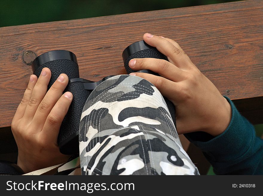 Child hands keep black binoculars on outlook-tower