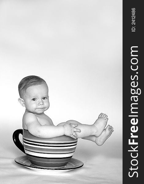 Black and white image of an adorable baby sitting in a colorful, over-sized teacup. Black and white image of an adorable baby sitting in a colorful, over-sized teacup