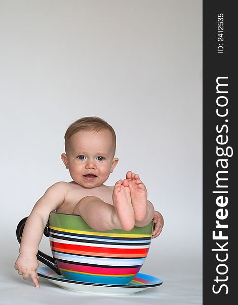 Image of an adorable baby sitting in a colorful, over-sized teacup. Image of an adorable baby sitting in a colorful, over-sized teacup