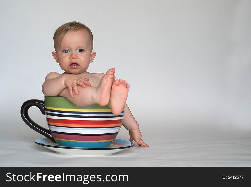 Image of an adorable baby sitting in a colorful, over-sized teacup. Image of an adorable baby sitting in a colorful, over-sized teacup