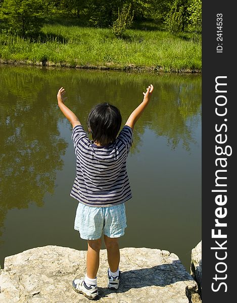 A child photographed from behind stands before a body of water with arms out in a welcoming or embracing position.