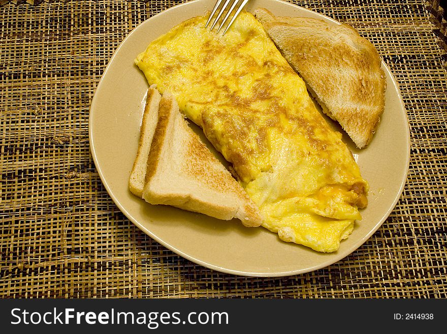 Omelette and white toast on a tan plate on a wicker placemat. Omelette and white toast on a tan plate on a wicker placemat