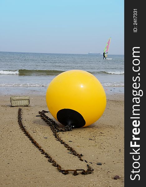 A yellow buoy sits on the beach with a windsurfer &  ship on the distant horizon. A yellow buoy sits on the beach with a windsurfer &  ship on the distant horizon