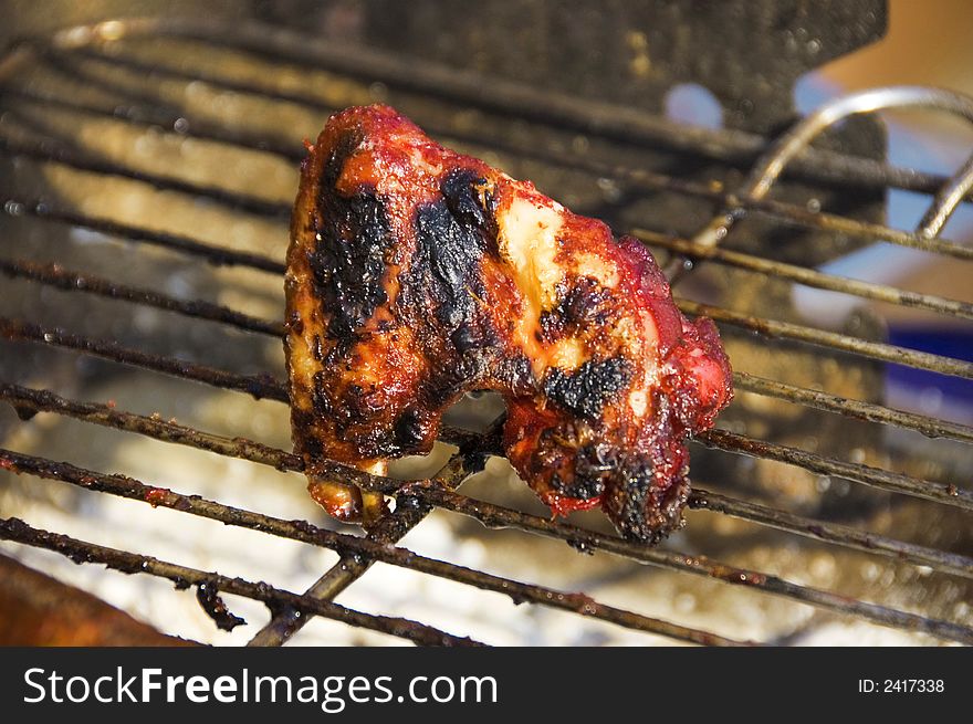 A sizzling piece of tandoori chicken cooks on a barbeque