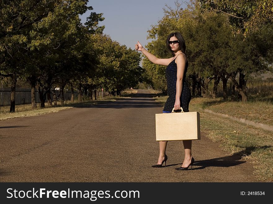 Brunette waiting for a lift standing roadside with thumb in air. Brunette waiting for a lift standing roadside with thumb in air