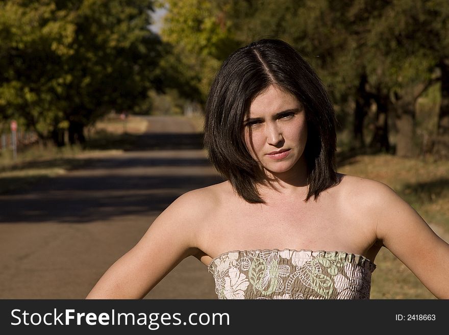 Closeup of beautiful and sexy brunette looking at the camera with a tree lane behind her. Closeup of beautiful and sexy brunette looking at the camera with a tree lane behind her