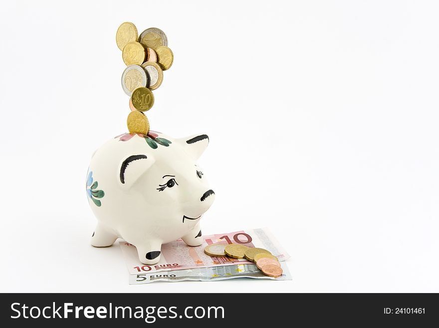 Coins falling into a piggy bank, which is depicted on banknotes, coins, on which lie on a white background.