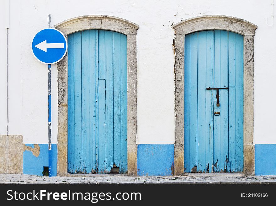 View of two old blue doors and a blue traffic sign. View of two old blue doors and a blue traffic sign.