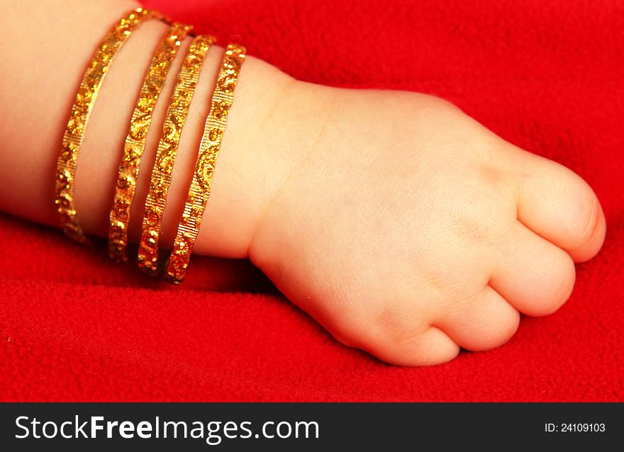 Baby hand, with golden bracelets, towards dark red