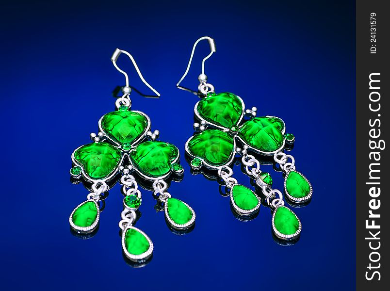 Earrings with green gemstone on a blue background. Earrings with green gemstone on a blue background