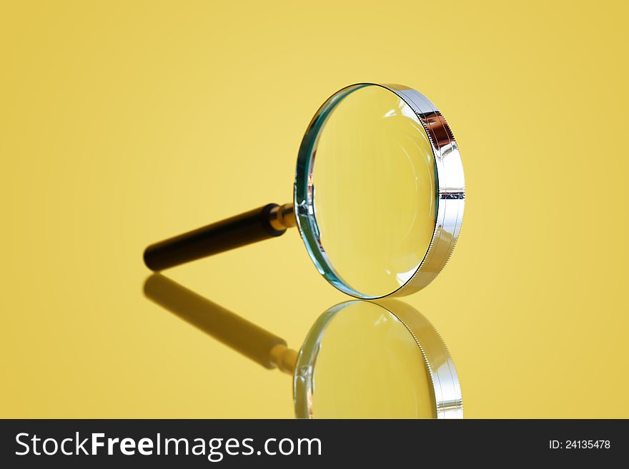 Closeup of magnifying glass on yellow background with reflection