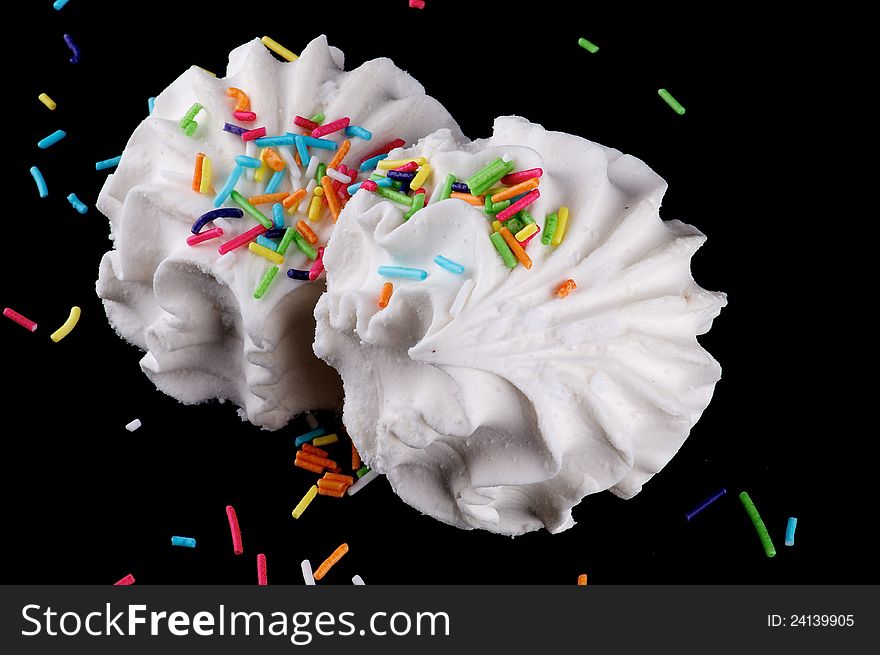 Two dessert marshmallows with coloured sugar grains isolated on black background