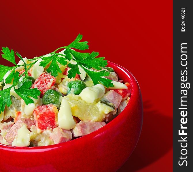 Salad with vegetables and sausage in a red cup in red background