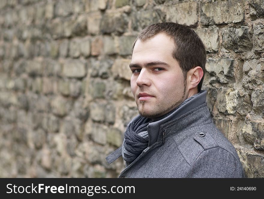 Young Man In Gray Coat Posing Near Old Wall