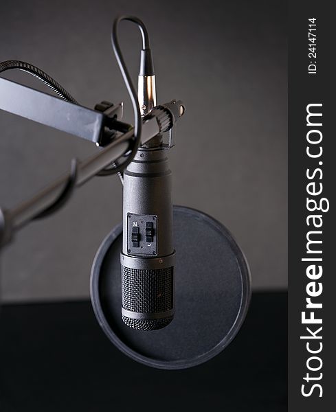 A professional studio microphone with a wind screen, on an artistic black background.