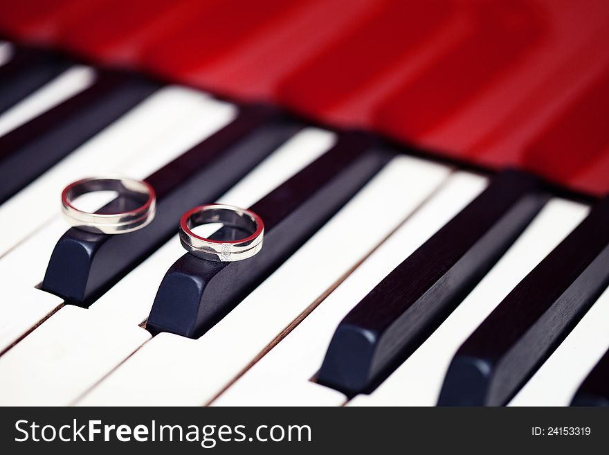 Silver wedding rings laying at the red piano keyboard. Silver wedding rings laying at the red piano keyboard