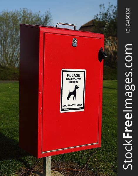 A red dogs waste bin located in a park. A red dogs waste bin located in a park