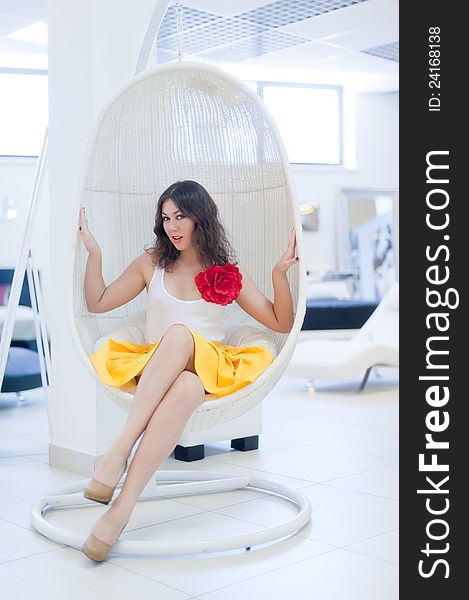 Picture an elegant young woman sitting in white hung seat somewhere in the fashionable interior. Picture an elegant young woman sitting in white hung seat somewhere in the fashionable interior