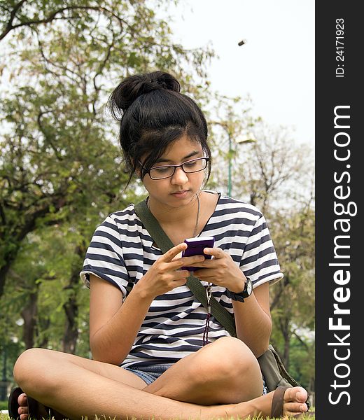 Woman sit on grass sending / receiving a text message / email on her mobile / cellular phone. Woman sit on grass sending / receiving a text message / email on her mobile / cellular phone.