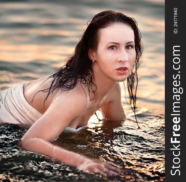 Portrait of a young girl lying in the sea in the light of the evening sun